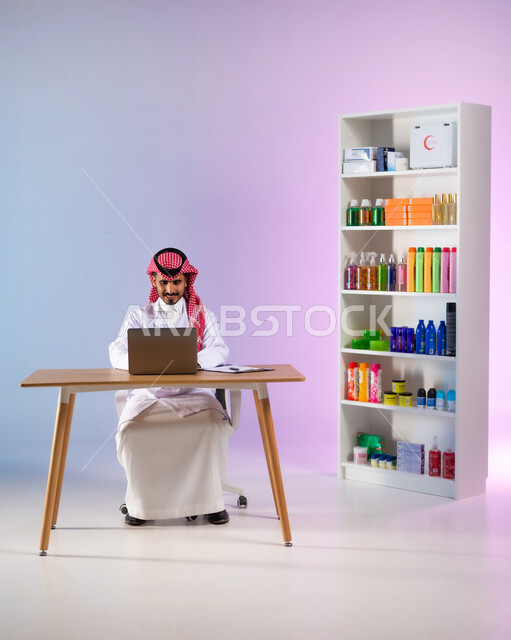 مفهوم الصيدلة واستخدام المنتجات الصحية, التسويق والترويج لمتسحضرات العناية بالبشرة, بورتريه لطبيب صيدلاني عربي خليجي سعودي مبتسم يرتدي المعطف الطبي الأبيض يقوم بالعمل على الحاسب المحمول في الصيدلية, البحث الطبي عن الوصفات العلاجية عبر الاونلاين, خلفية ملونة