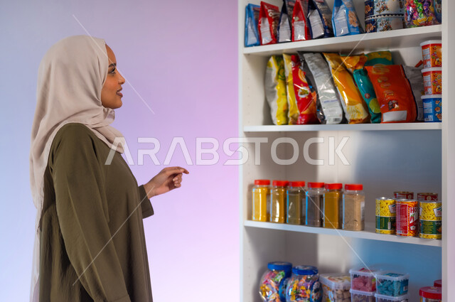 أنواع وأصناف من منتجات ومستلزمات المستهلك من مواد غذائيه مختلفه في المراكز التجاريه, الاستفادة من العروض والتخفيضات الموسمية على السلع, بورتريه مقرب من الجانب لإمرأة عربية خلجية سعودية محجبة ترتدي العباءة تقوم بالتسوق والتبضع من السوبرماركت, خلفية ملونة