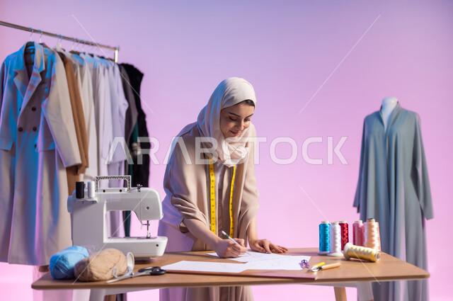 الابتكار و الإبداع في تصميم الأزياء , العمل في ورشة خياطة  , بورتريه مقرب لمصممة أزياء عربية خليجية سعودية ترتدي الزي الكاجوال و الحجاب تقوم برسم التصاميم على الورق  , خلفية ملونة