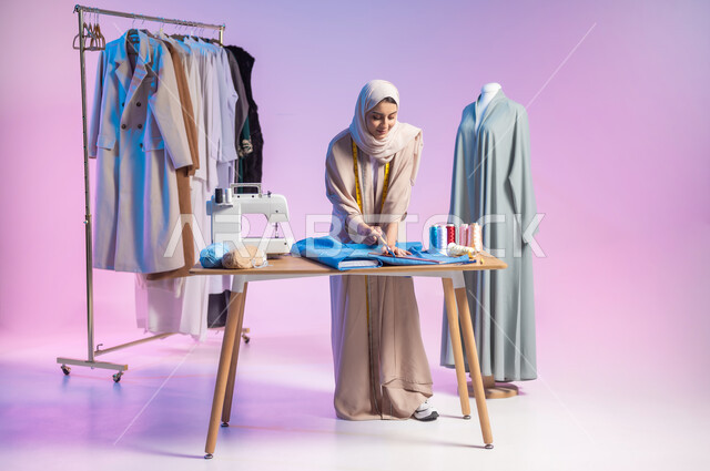 Fashion design workshop, practicing sewing, portrait of a Saudi Arabian Gulf fashion designer wearing casual clothes and the hijab, crafts and crafts in Saudi Arabia, full-length body photo, colored background