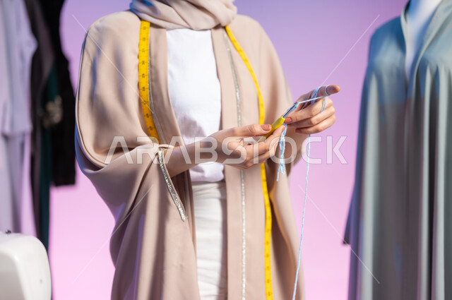 ممارسة مهنة الحياكة , خياطة و تفصيل الملابس النسائية في السعودية , بورتريه مقرب لمصممة أزياء عربية خليجية سعودية ترتدي الزي الكاجوال و الحجاب تمسك بيدها سنارة و خيط الصوف , حرف و مهن يدوية , خلفية ملونة