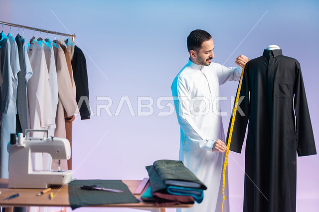 استخدام الشريط المتري لأخذ القياسات، ترتيب وتنسيق الثياب، استعمال أدوات ومعدات الخياطة، إتقان صنع الملابس السعودية، اختيار أجود أنواع الأقمشة لصناعة الأثواب، بورتريه مقرب لخياط عربي خليجي سعودي يرتدي الثوب التقليدي، مهن وحرف يدوية، خلفية ملونة