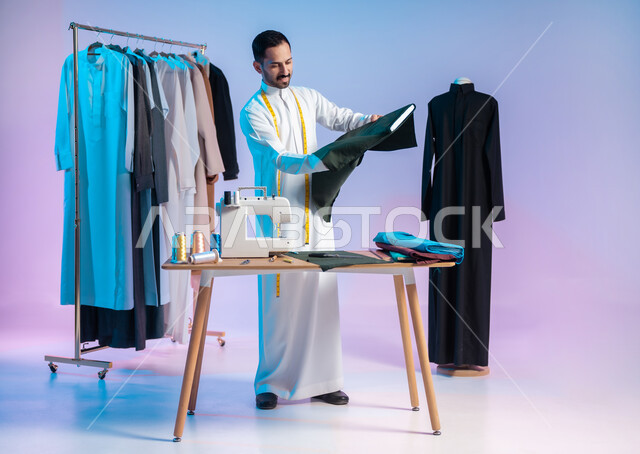 إتقان صنع الملابس السعودية، اختيار أجود أنواع الأقمشة لصناعة الأثواب، استعمال أدوات ومعدات الخياطة، بورتريه لخياط عربي خليجي سعودي يرتدي الثوب التقليدي يضع على رقبته الشريط المتري لأخذ القياسات، مهن وحرف يدوية، الجسم بالطول الكامل، خلفية ملونة
