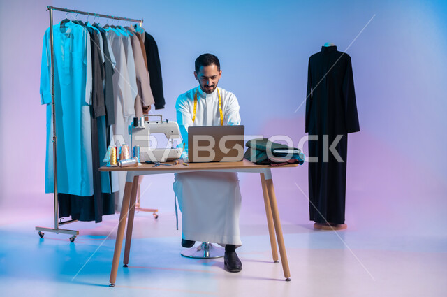 Creating wonderful designs and models, using modern and advanced technology, using sewing tools and equipment, mastering the making of Saudi clothes, a portrait of a Saudi Arabian Gulf tailor wearing a traditional dress, using a laptop, full-length body, colored background.