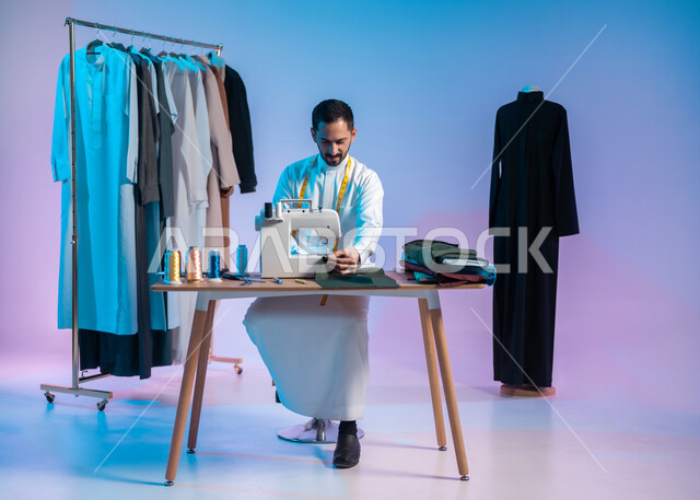 Using sewing tools and equipment, mastering the making of Saudi clothes, using a sewing machine to tailor clothes, a close-up portrait of a Saudi Arabian Gulf tailor wearing a traditional dress making dresses, a colored background