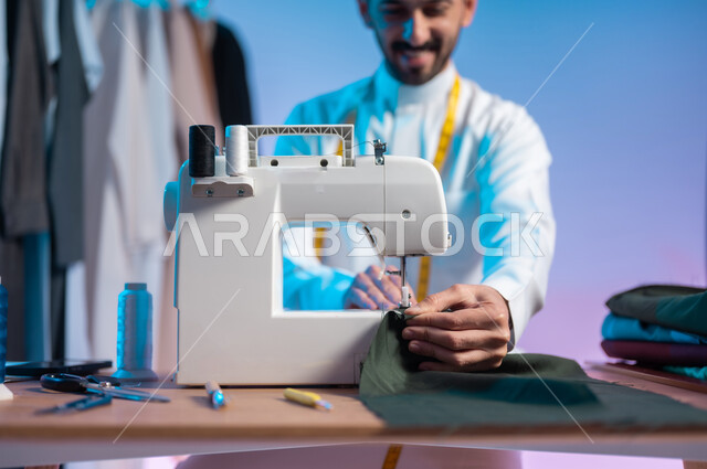 Using a sewing machine to tailor clothes, a close-up portrait of a Saudi Arabian Gulf tailor wearing a traditional thobe, making dresses, using sewing tools and equipment, mastering the making of Saudi clothes, a colorful background