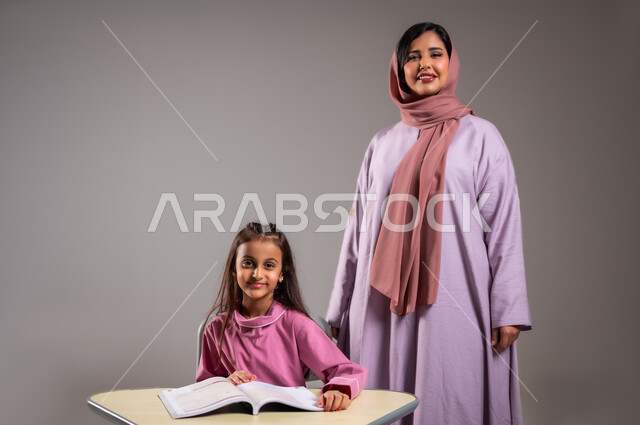 متعة التعلم في الفصل, معلمات المملكة العربية السعودية, بورتريه مقرب لمعلمة عربية سعودية خليجية تقوم بشرح الدروس لطالبة في المرحلة الإبتدائية في الفصل, أهداف التربية والتعليم بالمناهج المقررة للطلاب والطالبات, خلفية رمادية