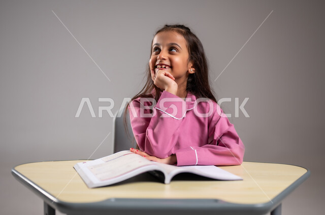 حل الاسئلة داخل الفصل الدراسي, ايماءات وتعابير التركيز والتفكير, بورتريه مقرب لطالبة عربية خليجية سعودية تجلس على المقعد الدراسي تفكر في حل السؤال, اهداف التربية و التعليم, خلفية رمادية