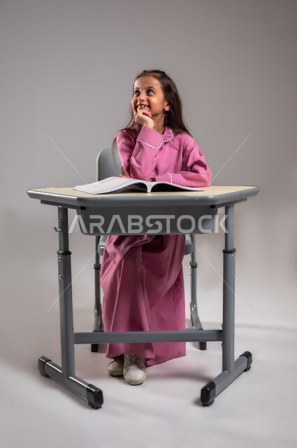 ايماءات وتعابير التركيز والاندماج بالدرس، التعليم والتربية بالمناهج المقررة للطلاب في المملكة العربية السعودية، بورتريه لطالبة عربية خليجية سعودية تجلس على المقعد الدراسي تفكر في حل السؤال، تلقي المعلومات داخل الفصل الدراسي , خلفية رمادية