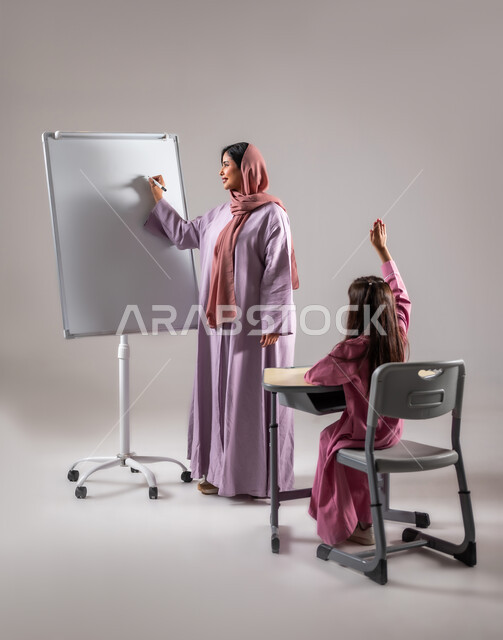 المشاركة والتفاعل داخل الفصل الدراسي، بورتريه لطالبة عربية خليجية سعودية ترفع يدها للإجابة على سؤال آنستها، التربية والتعليم بالمناهج المقررة للطلاب في المملكة العربية السعودية، تعابير وايماءات الحماس لمعرفة الجواب الصحيح, خلفية رمادية