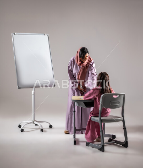 Achievement and success in the educational stages, goals of education in the curricula prescribed for male and female students in the Kingdom of Saudi Arabia, a Saudi Arabian Gulf teacher helping her student read and solve problems, using the white school board, gray background