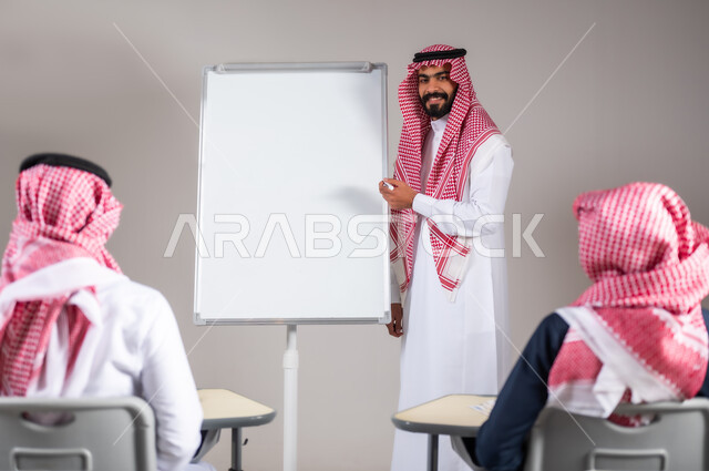 ايماءات التركيز و التمعن, أهمية العلم في تنمية القدرات العقلية,  بورتريه لمعلم عربي خليجي سعودي يرتدي الثوب التقليدي يشرح لطلابه الدرس على اللوح و الطلاب ينصتون اليه، خلفية رمادية