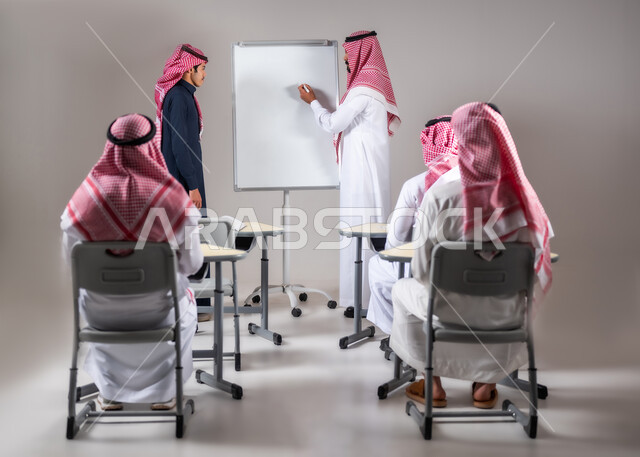 أهمية العلم في تنمية القدرات العقلية، نشاطات مدرسية جماعية،  بورتريه لطلاب  سعوديين جالسين على المقعد المدرسي يتلقون المعلومات من المعلم، ايماءات التركيز و التمعن بالدرس، خلفية رمادية