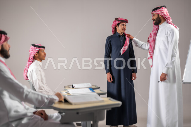 ايماءات البشاشة و السرور، بورتريه لمعلم عربي خليجي سعودي يرتدي الثوب التقليدي يضع يده على كتف الطالب بتعابير الرضا والمدح، التربية والتعليم بالمناهج المقررة للتلاميذ، مفهوم الاجتهاد و طلب التفوق، الانجاز و النجاح في المرحلة التعليمية، خلفية رمادية