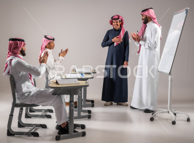 The concept of diligence and the pursuit of excellence, gestures of joy and happiness, a portrait of a Saudi Gulf Arab teacher wearing the traditional dress with an expression of satisfaction on his face for the students, effective participation in the class, education and teaching according to the curricula prescribed for the students, success in the educational stage, gray background