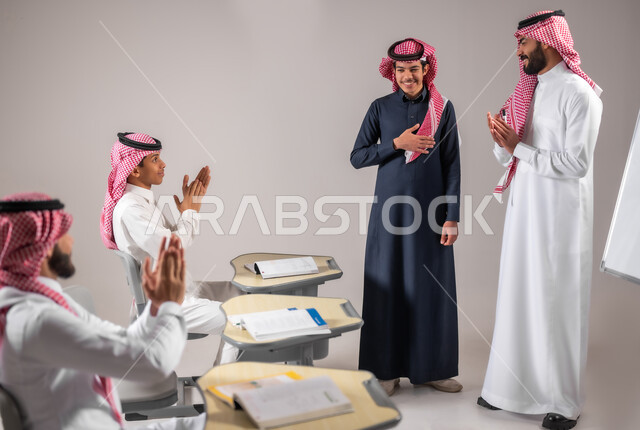 ايماءات التشجيع والتصفيق داخل الفصل الدراسي، بورتريه لمعلم عربي خليجي سعودي يرتدي الثوب التقليدي ينظر الى طالبه بتعابير الرضا والسرو، المشاركة الفعالة في الصف، التربية والتعليم بالمنهاج المقررة، خلفية رمادية