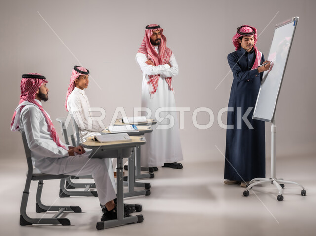 التربية والتعليم بالمنهاج المقررة، المشاركة الفعالة في الصف، الانجاز و التفوق في المرحلة التعليمية، بورتريه لطالب عربي خليجي سعودي يرتدي الثوب التقليدي يقوم بالشرح والإجابة على سؤال المعلم امام التلاميذ، استخدام اللوحة المدرسية البيضاء، خلفية رمادية