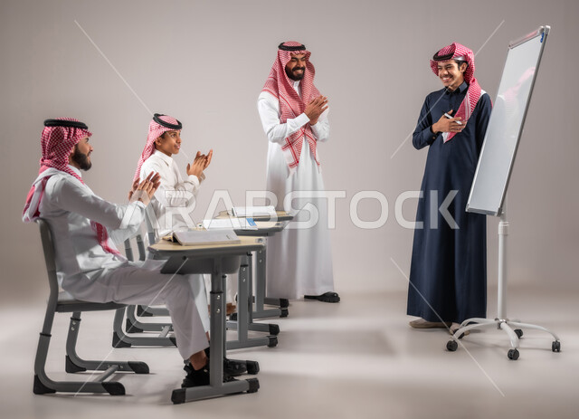 المشاركة الفعالة في الصف ايماءات التشجيع  و التصفيق داخل الفصل الدراسي، بورتريه لطالب عربي خليجي سعودي يرتدي الثوب التقليدي يقوم بالشرح والإجابة على سؤال المعلم امام التلاميذ، استخدام اللوحة المدرسية البيضاء، التربية والتعليم بالمنهاج المقررة، خلفية رمادية