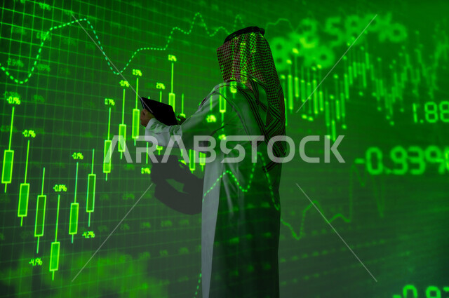 النجاح في التداول المالي , استخدام التقنيات الحديثة و المتطورة , رجل عربي خليجي سعودي يرتدي الثوب التقليدي و الشماغ يقف أمام شاشة مليئة بالأرقام و الإحصائيات يقوم بالاطلاع على الرسم البيانية عبر الجهاز اللوحي , عرض شاشة سوداء فارغة عبر التابلت, خلفية هولوجرامية ثلاثية الأبعاد