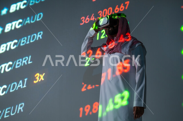 تطورات سوق الأوراق المالية , متابعة صعود و هبوط الأسهم , رجل عربي خليجي سعودي يرتدي الثوب التقليدي و الشماغ يقف أمام شاشة مليئة بالأرقام و الإحصائيات يضع نظارة الفي ار , ارتداء نظارات العالم الافتراضي  , خلفية هولوجرامية ثلاثية الأبعاد