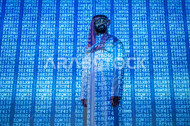 العمل في تطوير الأنظمة البرمجية , مفهوم الأمن السيبراني , رجل عربي خليجي سعودي يرتدي الثوب التقليدي و الشماغ , رموز و أكواد تشير لبيانات محمية , خلفية هولوجرامية ثلاثية الأبعاد