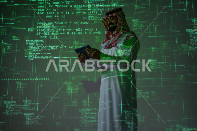 تطوير مواقع الويب و التطبيقات , مفهوم لغات و خوارزميات البرمجة , رجل عربي خليجي سعودي يرتدي الثوب التقليدي و الشماغ يمسك الجهاز اللوحي بيديه , استخدام التقنيات الحديثة , خلفية هولوجرامية ثلاثية الأبعاد