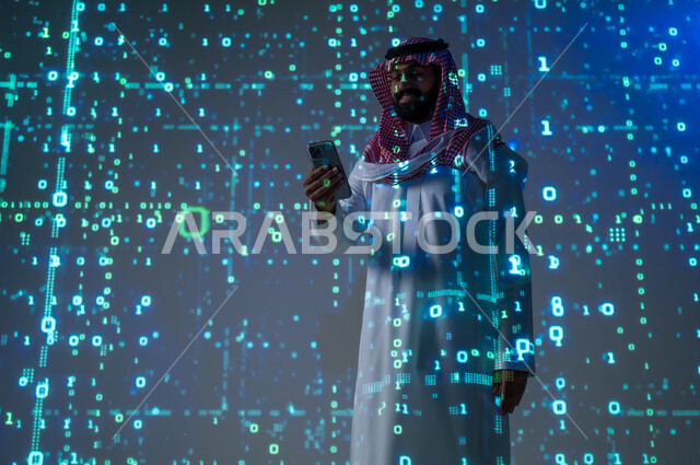 التواصل مع الأهل و الأصدقاء , مفهوم التطور التقني , رجل عربي خليجي سعودي يرتدي الثوب التقليدي و الشماغ يمسك هاتفه المحمول بيده , استخدام الأجهزة الحديثة , خلفية هولوجرامية ثلاثية الأبعاد