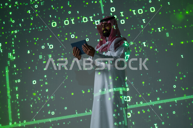 استخدام التقنيات المتطورة , التقدم التقني في السعودية , رجل عربي خليجي سعودي يرتدي الثوب التقليدي و الشماغ  يمسك الجهاز اللوحي بيديه , خلفية هولوجرامية ثلاثية الأبعاد