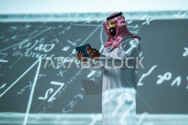 استخدام الأجهزة المتطورة , التقدم العلمي و التقني  , رجل عربي خليجي سعودي يرتدي الثوب التقليدي و الشماغ يمسك الجهاز اللوحي بيديه , أرقام و قوانين رياضية , خلفية هولوجرامية ثلاثية الأبعاد