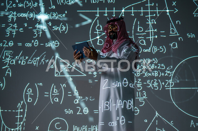 استخدام الأجهزة الذكية الحديثة، التطور العلمي والتقني في المملكة العربية السعودية، دمج العلم بالتكنولوجيا في مادة الرياضيات، شاب عربي خليجي سعودي يرتدي الثوب التقليدي والشماغ يعمل من خلال جهاز لوحي يقف أمام المعادلات والقوانين الرياضية، الخلفية قوانين وخوارزميات رياضية