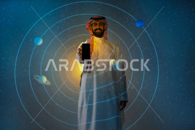 Digital and technological development, a Saudi future vision 2030, the growth of the space sector in the Kingdom of Saudi Arabia, a young Saudi Arabian Gulf man wearing a traditional dress standing between the planets and stars holding a mobile phone in his hand, displaying a blank black screen, a 3D holographic background of the movement of the planets around the sun