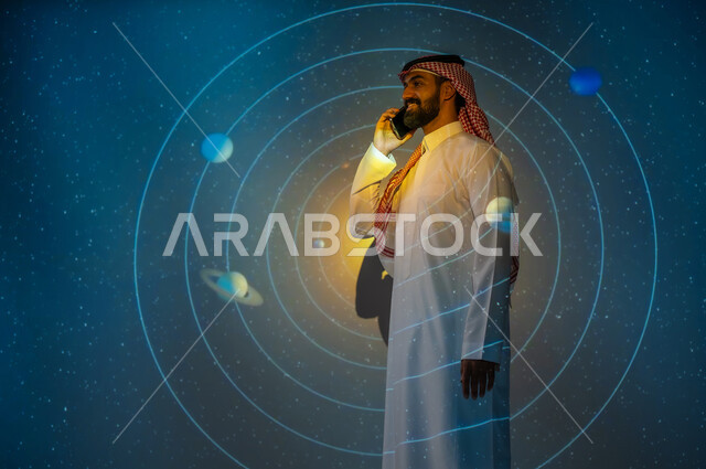 رؤية مستقبلية سعودية ٢٠٣٠، نمو قطاع الفضاء في المملكة العربية السعودية، التطور الرقمي والتكنولوجي، شاب عربي سعودي خليجي مبتسم يرتدي الثوب التقليدي يقف بين الكواكب والنجوم يقوم بالتحدث عبر الهاتف المحمول، خلفية هيولوجرامية ثلاثية الأبعاد لحركة الكواكب حول الشمس