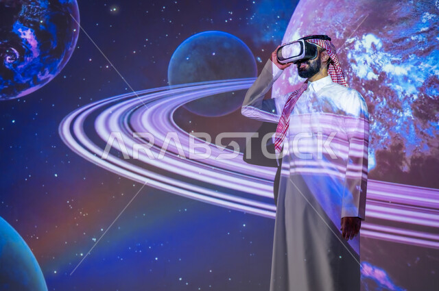 نمو قطاع الفضاء في المملكة العربية السعودية، التطور الرقمي والتكنولوجي، شاب عربي سعودي خليجي يرتدي الثوب التقليدي مبتسم يقف بين الكواكب والنجوم ينظر من خلال نظارات الفي ار، رؤية مستقبلية سعودية ٢٠٣٠، خلفية هيولوجرامية ثلاثية الأبعاد للكواكب