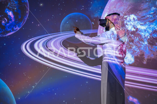 التطور الرقمي والتكنولوجي، نمو قطاع الفضاء في المملكة العربية السعودية، شاب عربي سعودي خليجي يرتدي الثوب التقليدي مبتسم يقف بين الكواكب والنجوم ينظر من خلال نظارات الفي ار، رؤية مستقبلية سعودية ٢٠٣٠، خلفية هيولوجرامية ثلاثية الأبعاد للكواكب