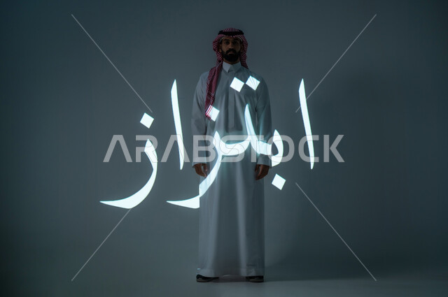 مخطوطة كلمة ابتزاز باللغة العربية، بورتريه شاب عربي خليجي سعودي يرتدي الثوب التقليدي ويضع الشماغ، الطول الكامل للجسم، خلفية رمادية