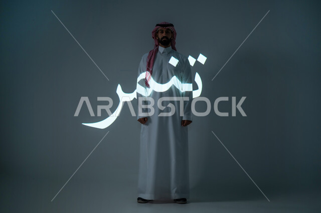 Manuscript of the word “bullying” in Arabic, portrait of a Saudi Gulf Arab young man wearing a traditional dress and wearing a shemagh, full length of the body, gray background