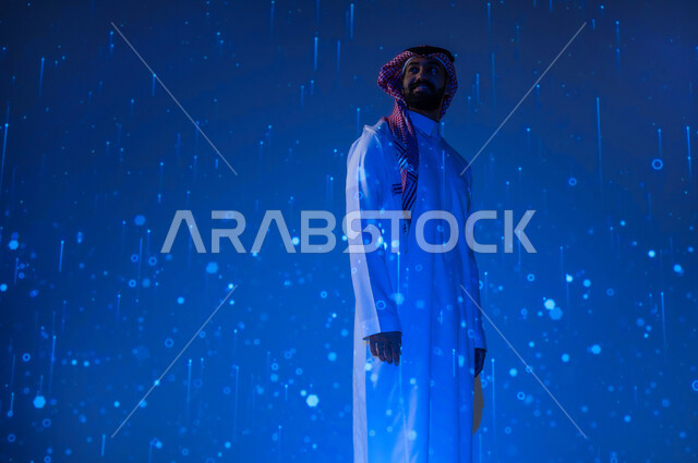 التطور التكنولوجي والرقمي في المملكة العربية السعودية، شاب عربي سعودي خليجي يرتدي الثوب التقليدي مبتسم ينظر إلى الأعلى بايماءات السعادة والفخر، رؤية مستقبلية سعودية ٢٠٣٠، خلفية هيولوجرامية ثلاثية الأبعاد لخطوط ونقاط مضيئة