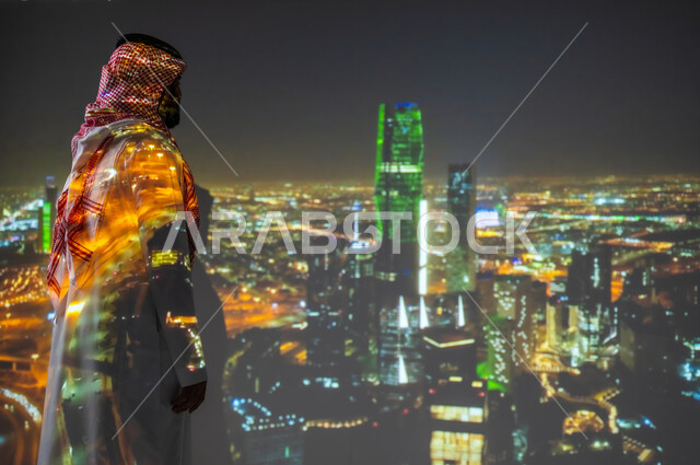 ذكرى اليوم الوطني للسعودية في 23 سبتمبر، الاحتفال بالأعياد والمناسبات الوطنية، رجل عربي خليجي سعودي مبتسم يرتدي الزي التقليدي يقف بجانب علم المملكة العربية السعودية يحتفل يوم العلم السعودي في11 مارس، الخلفية مركز الملك عبدالله المالي في الرياض