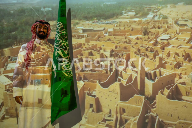 الاحتفال بيوم العلم السعودي في11 مارس، ذكرى يوم الاستقلال للسعودية في 23 سبتمبر، الأعياد والمناسبات الوطنية، شاب عربي خليجي سعودي مبتسم يرتدي الزي التقليدي ينظر إلى الكاميرا ويقف بجانب علم المملكة العربية السعودية، الخلفية قصر سلوى الدرعية البجيري في الرياض