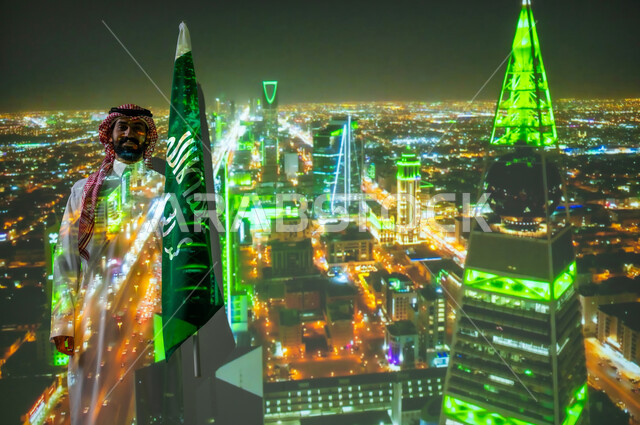 الاحتفال بالأعياد والمناسبات الوطنية، ذكرى اليوم الوطني للسعودية في 23 سبتمبر، رجل عربي خليجي سعودي مبتسم يرتدي الزي التقليدي يقف بجانب علم المملكة العربية السعودية يحتفل يوم العلم السعودي في11 مارس، الخلفية برج الفيصلية في الرياض