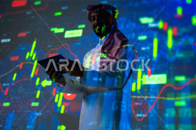 استخدام التقنيات لمراقبة الاقتصاد و معلومات الاستثمارات المالية, جمع بيانات البورصة وسوق الأسهم, رجل عربي خليجي سعودي يرتدي الثوب التقليدي و الشماغ ينظر الى الكاميرا يمسك بيده جهاز التابلت يقف أمام شاشة مليئة بالأرقام, خلفية هولوجرامية ثلاثية الأبعاد