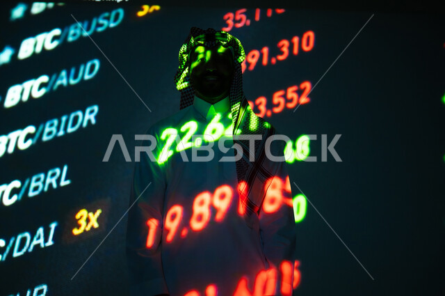مراقبة البورصة و البيانات الاقتصادية , سوق الأوراق المالية, رجل عربي خليجي سعودي يرتدي الثوب التقليدي و الشماغ ينظر الى الكاميرا بإيماءات الثقة بالنفس يقف أمام شاشة مليئة بالأرقام و الإحصائيات, خلفية هولوجرامية ثلاثية الأبعاد