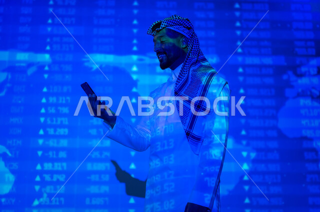 التغيرات العالمية بأسعار أسهم البورصة , صورة من الخلف لرجل عربي خليجي سعودي يرتدي الثوب التقليدي و الشماغ يقف أمام شاشة مليئة بالأرقام و الإحصائيات يمسك بيده الهاتف المحمول, خلفية هولوجرامية ثلاثية الأبعاد لخريطة العالم باللون الأزرق