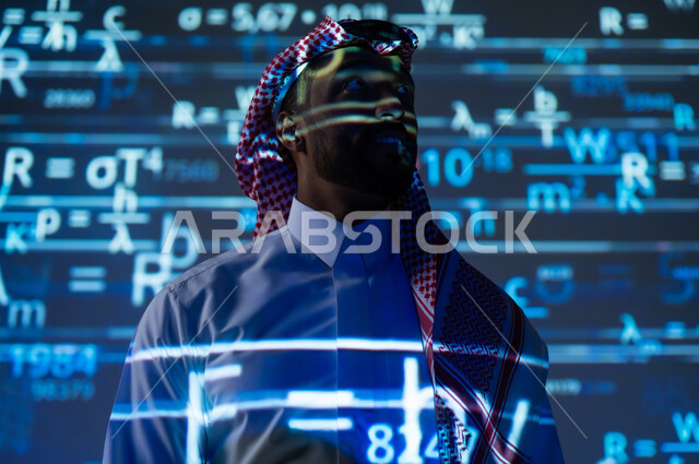 أرقام وحسابات في مادة الرياضيات، رجل عربي خليجي سعودي يرتدي الثوب التقليدي والشماغ يقف باستقامة ينظر الى شيء ما بإيماءات السرور, التطور العلمي و التقني في المملكة العربية السعودية, خلفية زرقاء للقوانين والمعادلات