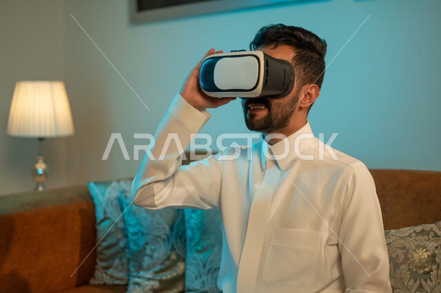 التفاعل و المتعة و التسلية بمتابعة المسلسلات ، مشاهدة أفلام ثلاثية الابعاد عبر نظارة الواقع الإفتراضي الحديث ، شاب عربي خليجي سعودي يرتدي نظارات العالم الخيالي , التطور والتقدم التقني والتكنولوجي , إيماءات وجه ويدين تدل على الحماس