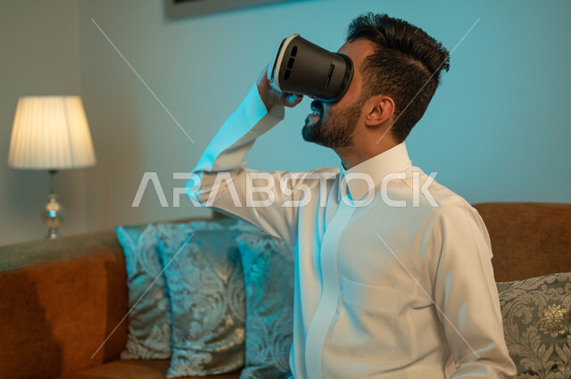 مشاهدة أفلام ثلاثية الابعاد عبر نظارة الواقع الإفتراضي الحديث ، التفاعل و المتعة و التسلية بمتابعة المسلسلات ، شاب عربي خليجي سعودي يرتدي نظارات العالم الخيالي , التطور والتقدم التقني والتكنولوجي , إيماءات وجه ويدين تدل على الحماس