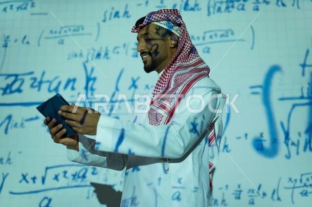 دمج العلم بالتكنولوجيا، أرقام وحسابات في مادة الرياضيات، رجل عربي خليجي سعودي يرتدي الثوب التقليدي والشماغ يحمل بيده جهار لوحي , التطور العلمي و التقني في المملكة العربية السعودية, استخدام التقنيات الحديثة, خلفية قوانين ومعادلات رياضية