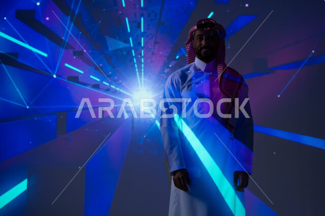 تعزيز مفهوم التقدم التكنولوجي والتطور في المجتمع السعودي، التقنيات الحديثة والمتطورة، الاهتمام بالقطاع الالكتروني في المملكة العربية السعودية، شاب عربي خليجي سعودي يرتدي الثوب التقليدي ينظر إلى الكاميرا بايماءات السعادة، رؤية مستقبلية ٢٠٣٠، الخلفية إضاءة النيون الزرقاء