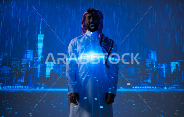 ايماءات السعادة والبهجة، مشاهدة فصل الشتاء الماطر، الأجواء الممطرة في المملكة العربية السعودية، رؤية سعودية مستقبلية٢٠٣٠، شاب عربي سعودي خليجي يرتدي الزي التقليدي والشماغ يقف تحت المطر أمام الأبراج وناطحات السحاب وينظر إلى الكاميرا، زيارة الأماكن المحلية