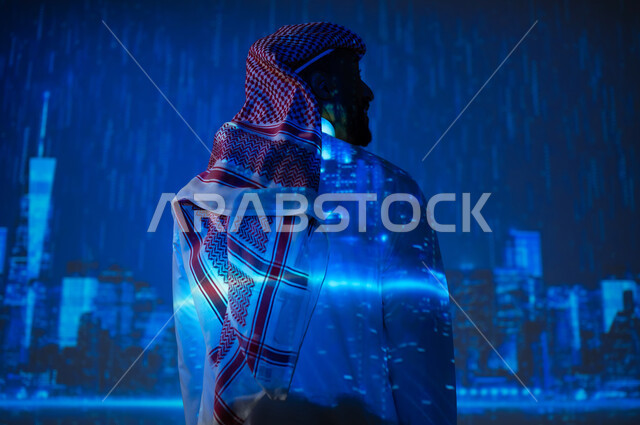 الأجواء الممطرة في المملكة العربية السعودية، مشاهدة فصل الشتاء الماطر، شاب عربي سعودي خليجي يرتدي الزي التقليدي والشماغ يقف تحت المطر ينظر إلى الأبراج وناطحات السحاب، زيارة الأماكن المحلية
